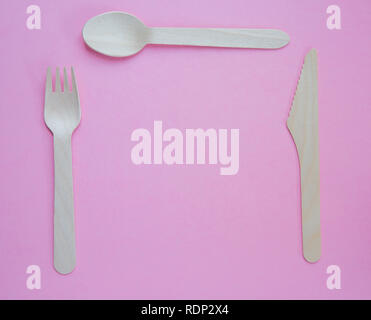 A flat lay of sustainable wooden cutlery including a knife, fork and spoon set for dinner in a place setting and on a pink background wit copy space Stock Photo