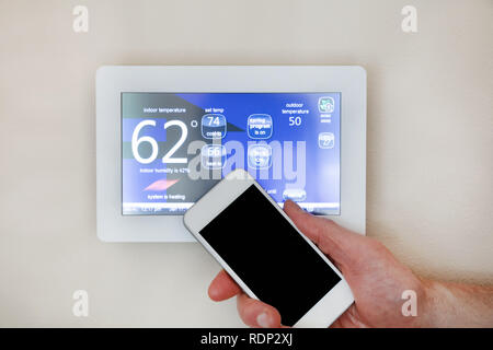 Male hand holding smart phone to operate heating or cooling of thermostat for home Stock Photo
