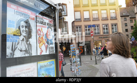 STRASBOURG, FRANCE - MAY 5, 2018: Woman reading newspaper covers in French city of Strasbourg on a press kiosk advertising wall Charlie Hebdo with Kim Jong-un Supreme Leader of North Korea on cover   Stock Photo