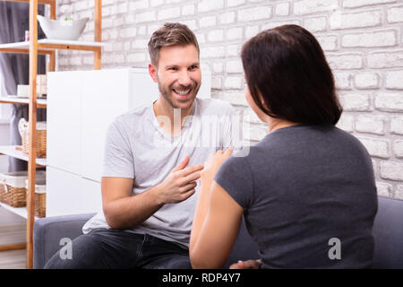Smiling Young Couple Sitting On Sofa Communicating With Sign Language Stock Photo