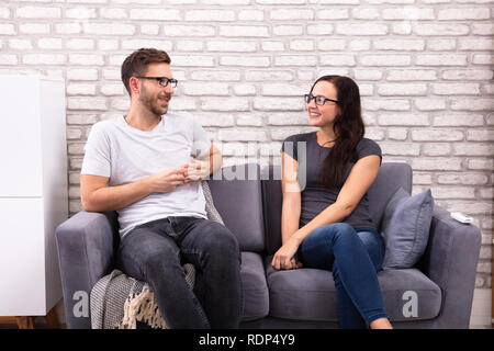 Young Men And Woman Sitting On Sofa Looking At Each Other During Date Stock Photo