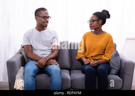 An African Young Couple Sitting On Sofa Looking At Each Other Stock Photo