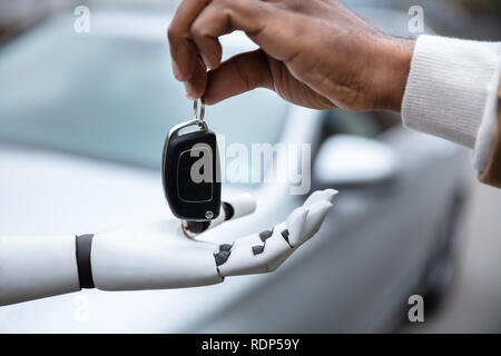Close-up Of A Man's Hand Giving Car Key To Robot Stock Photo