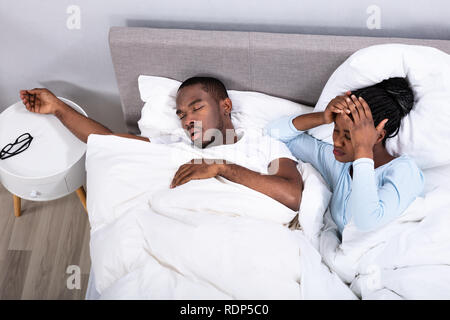 Disturbed African Woman Covering Her Ears While Her Husband Snoring On Bed Stock Photo