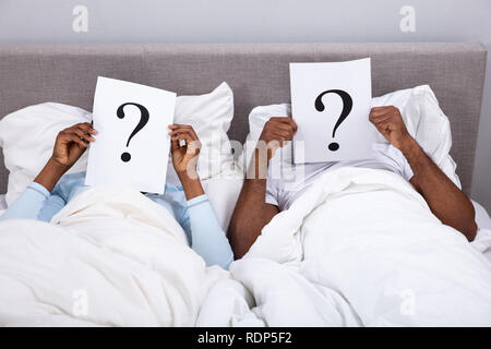 Couple Lying On Bed Holding Question Mark Sign In Front Of Their Face Stock Photo