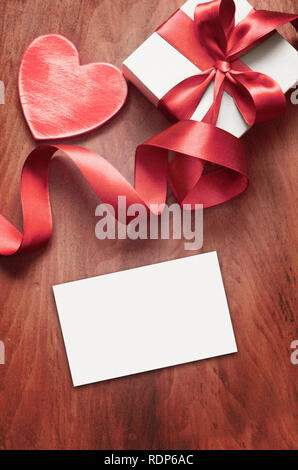 White gift box and red ribbon with tag on wood background with space. Vintage gift box on wooden board with space for text. Stock Photo