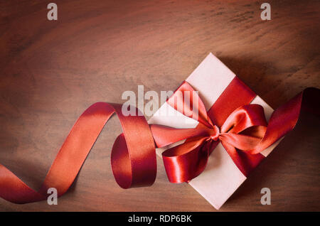 White gift box and red ribbon with tag on wood background with space. Vintage gift box on wooden board with space for text. Stock Photo