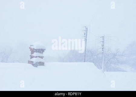 Chimney in red bricks and two antennas with white snow on roof. Stock Photo