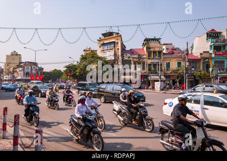 Busy intersection with several cars, mopeds and motorbikes on the road in afternoon light, Hanoi, Vietnam Stock Photo