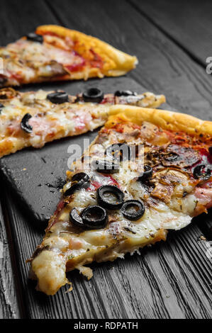 pieces of pizza on dark black wooden board, traditional italian pizza Stock Photo