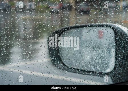 Drops of rain on the window and on the wing mirror; wet pavement in the background; shallow depth of field Stock Photo