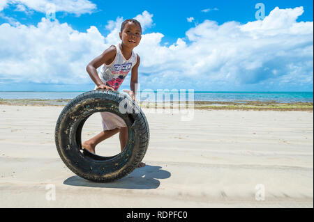 CAIRU, BRAZIL - FEBRUARY 15, 2017: A young Brazilian rolls a tire as a game along a an empty beach on a remote island in rural Bahia. Stock Photo