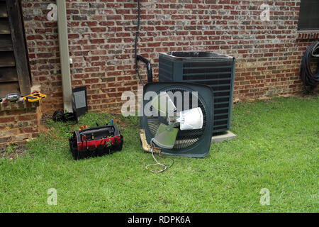 Air Conditioner compressor condenser coil with fan and tools being worked on next to a brick house for repair maintenance. Stock Photo