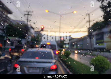 Rainy drops on car front window with blur traffic jam in evening. Stock Photo