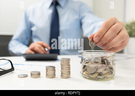 Man calculates the savings. Budget planning concept. Businessman working in the office. Man puts coins into the jar Stock Photo