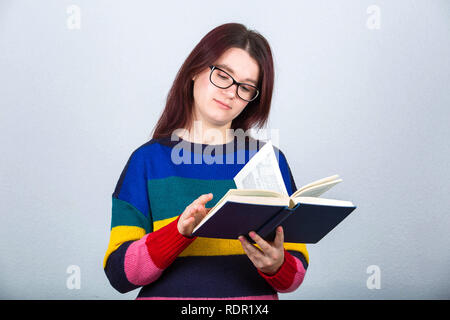 Serious young student girl wearing glasses reading a book isolated over grey wall background. Stock Photo