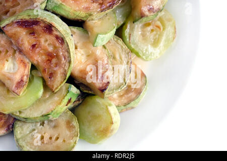 Many fried zucchini slices on round white plate over white background studio shot top view closeup Stock Photo