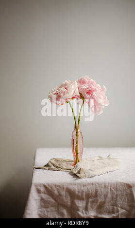 Two peonies in a pink fish-shaped vase on a crumpled linen tablecloth Stock Photo