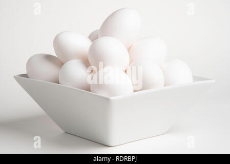 A bunch of white raw eggs stacked on a deep square bowl set against a plain white background in horiontal image format. Stock Photo