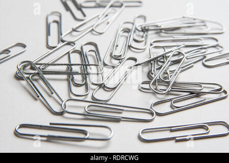 A close-up with selective focus of a bunch of metal paper clips scattered on a plain white background in horizontal image format. Stock Photo