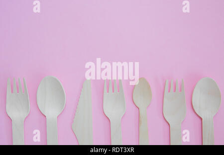 A flat lay of a variety of sustainable and environmentally friendly wooden cutlery including knife, fork and spoon with copy space on a pink backgroun Stock Photo