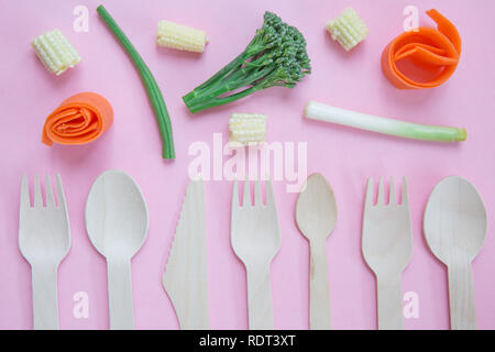 A flat lay of a variety of sustainable and environmentally friendly wooden cutlery including knife, fork and spoon with healthy vegetarian food Stock Photo