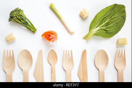 A flat lay of a variety of sustainable and environmentally friendly wooden cutlery including knife, fork and spoon with fresh vegan vegetables Stock Photo