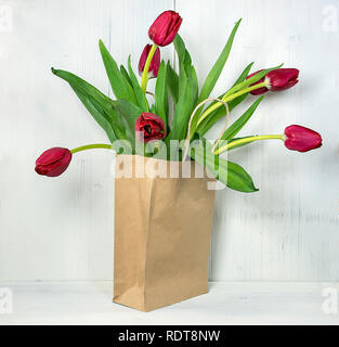 red tulips in generic brown paper bag on rustic whitewashed wood Stock Photo
