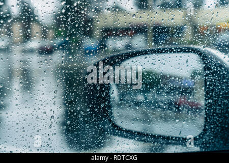 Drops of rain on the window and on the wing mirror; wet pavement in the background; Stock Photo