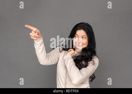 Freestyle. Mature lady standing isolated on grey pointing aside cheerful Stock Photo