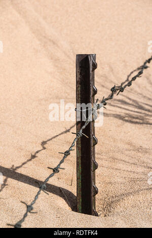 Barbed wire fence with metal posts nearly buried in sand Stock Photo