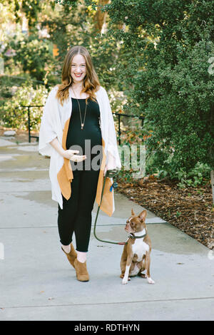 A dog walking woman holds her belly and walks next to her pet dog is smiling and happy Stock Photo