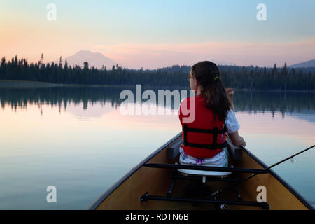 Girl paddling canoe on Hosmer Lake at dusk, Mountain Bachelor in background, Cascade Lakes, Oregon, USA