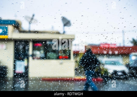 Raindrops on the windshield; Person walking outside during rainy weather in the background; California Stock Photo