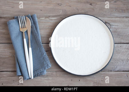 Natural table setting - plain ceramic plate, linen napkin, cutlery on wooden table. Eco-friendly concept, nordic style. Stock Photo