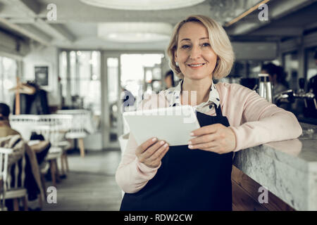 Blonde-haired entrepreneur owing restaurant holding little white tablet Stock Photo