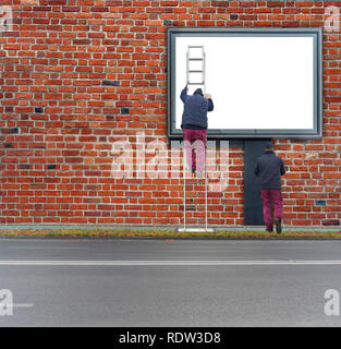 Working man on big black billboard in the city with red brick wall background Stock Photo