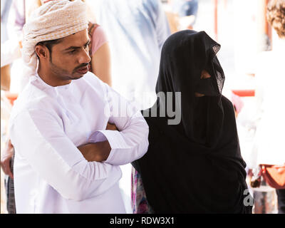 Nizwa, Oman - November 2, 2018: Omani couple in traditional clothes with a woman wearing a veil and a mask at the Friday market in Nizwa Stock Photo