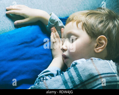 Little blonde boy sleeping under a blanket on blue pillow Stock Photo