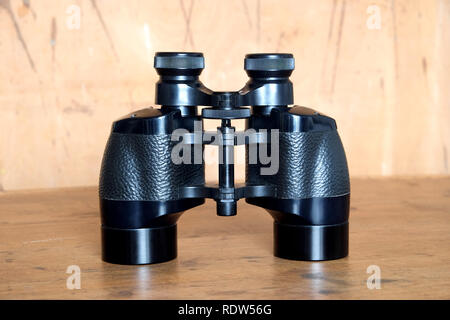 Vintage english military Porro prism black color binoculars on wooden background front view close up Stock Photo