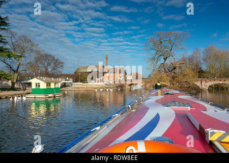 man stands on front of boat in bright sunlight during winter in the UK with ancient buildings and bridges in the background Stock Photo