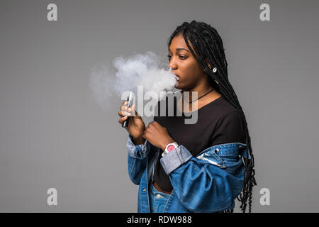 Side view portrait of guy holding vape device and exhaling cloud of smoke isolated on blue background. Stock Photo