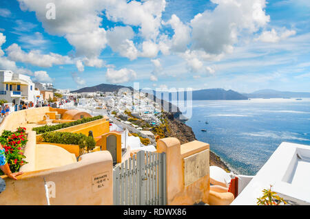 A scenic view of the Santorini caldera and the Aegean Sea from a resort terrace as tourists walk the main street in the hillside village of Oia, Greec Stock Photo