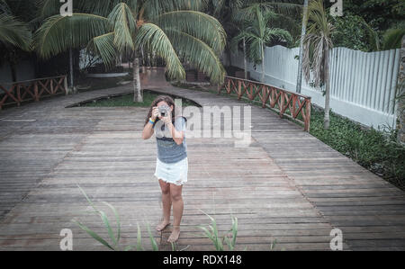 Young woman  taking photos in from wooden pier with nice palm trees in the back Stock Photo
