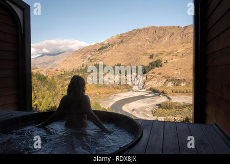 A woman (model released) relaxes in a hot tub while enjoying views of the Shotover River at the Onsen Hot Pools near Queenstown, New Zealand. Stock Photo