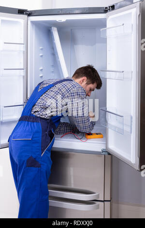 Young Serviceman Checking Fridge With Digital Multimeter Stock Photo
