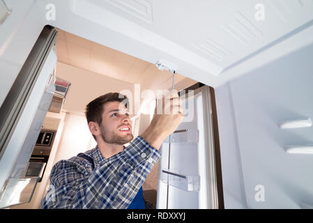 Young Male Technician Checking Refrigerator With Screwdriver Stock Photo
