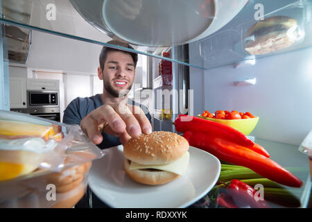 Smiling Young Man Touching The Burger In Refrigerator Stock Photo