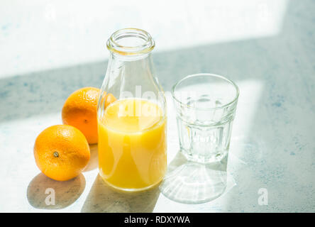 Freshly squeezed orange juice in a bottle. An empty glass and whole oranges are on side. Stock Photo