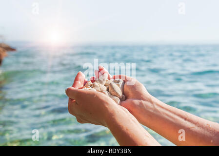 Female hands on the background of sea or ocean are holding sea stones. Stock Photo